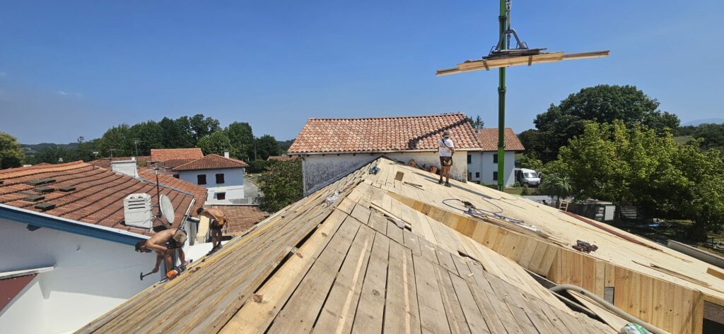 Artisans en train de rénover la charpente de l'école Saint-Laurent d'Arbonne pendant l'été 2026